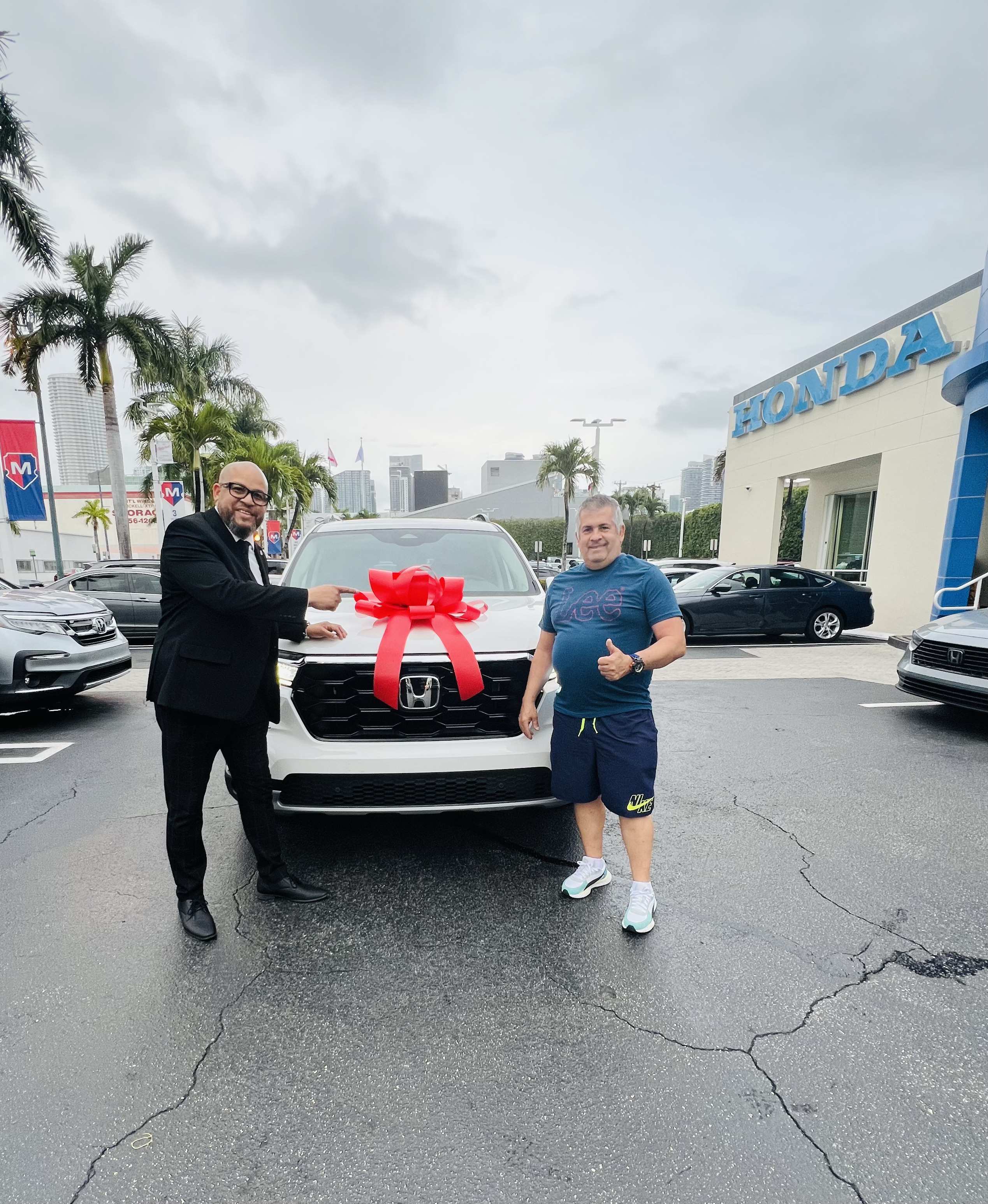Alexander Montalvo con un cliente satisfecho junto a su Honda nuevo con lazo rojo en Miami