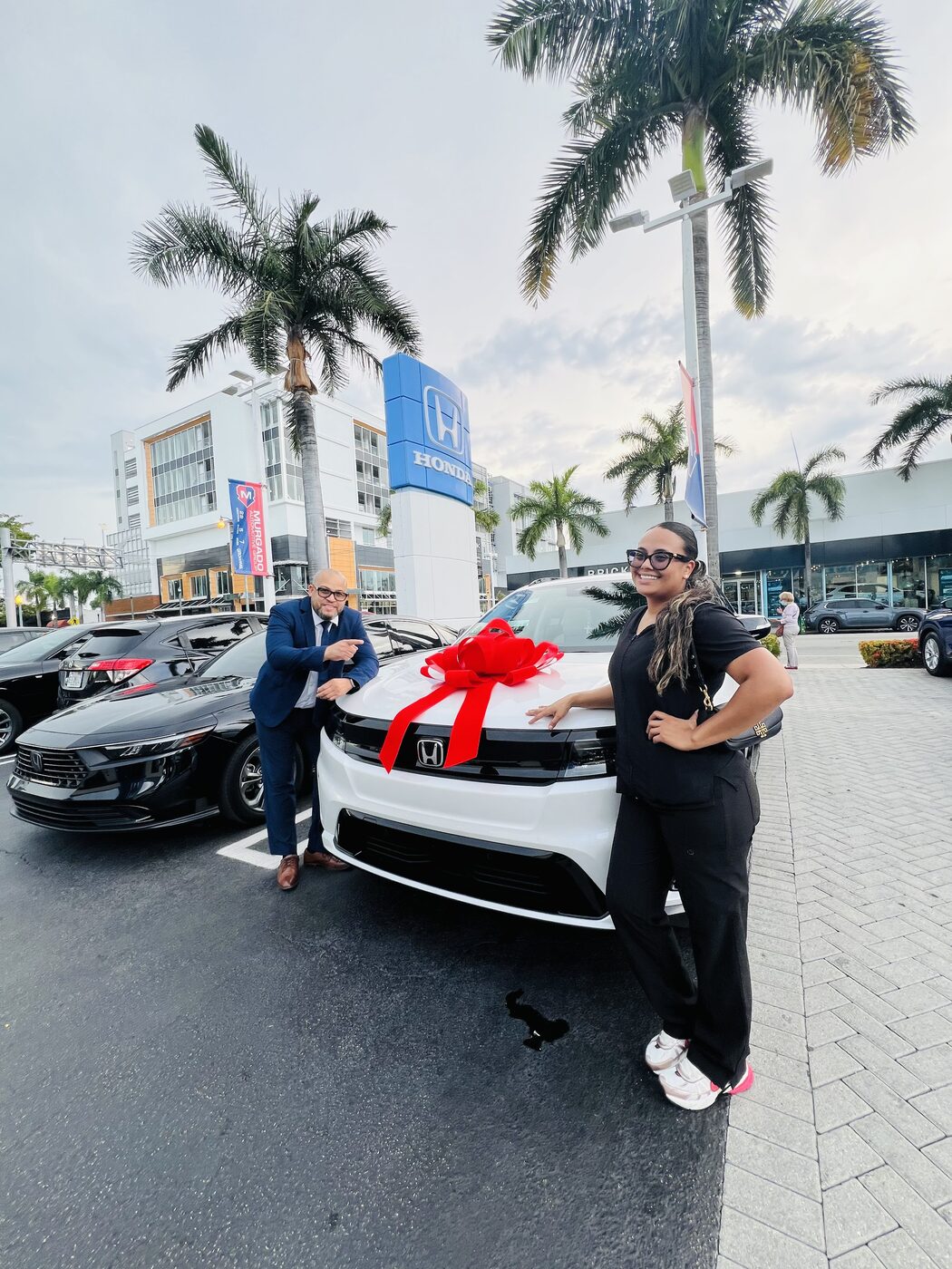 Clienta junto a su sedán blanco nuevo con lazo rojo en Miami